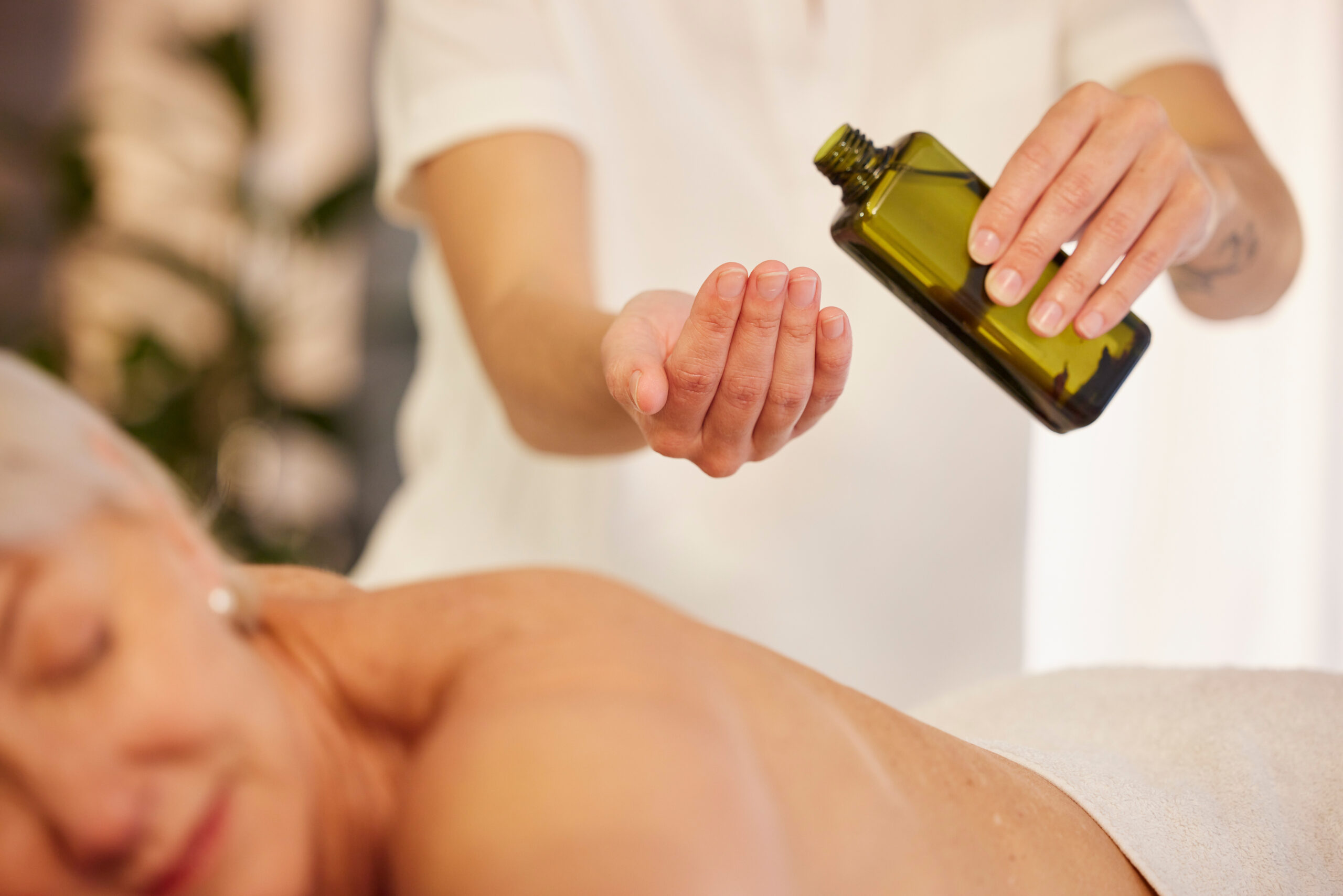 Massage, oil and a therapist with a woman at a spa to relax with wellness and skincare service. Hands, bottle and a masseuse with stress relief treatment for a patient body or person at a hotel Deluxe Paket
